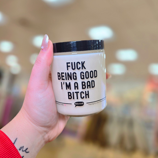 Hand holding a candle with text 'Fuck being good I'm a bad bitch' against a blurred background